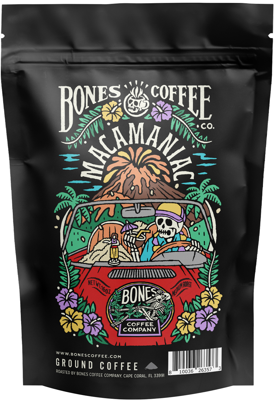 The front of a 4 ounce bag of Bones Coffee Company Macamaniac coffee. Its flavor is macadamia nut and coconut, and it has a skeleton driving a red car drinking from a coconut as it drives away from a volcano on the art.