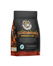 The back of a 12 ounce flavored coffee bag named Crusader’s Cup. The Rain Forest Alliance page on the lower left of the back of the bag, and it says to squeeze and sniff at the top of the bag. Below the squeeze and sniff text is the name Crusader’s Cup.