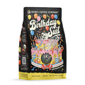 The front of a 12 ounce bag of Bones Coffee Company Birthday Suit coffee. Its flavor is birthday cake, and it has a skeleton laying on a birthday cake with a birthday hat on blowing into a streamer on the front.