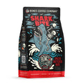 The front of a 12 ounce flavored coffee bag named Shark Bite. It showcases a skeleton riding on a shark missing an arm, and in the shark's jaws is a skeletal arm on its art.
