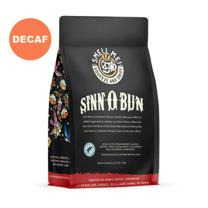 The back of a 12 ounce flavored coffee bag named Sinn-O-Bun. The Rain Forest Alliance page on the lower left of the back of the bag, and it says to squeeze and sniff at the top of the bag. Below the squeeze and sniff text is the name Sinn-O-Bun. A sticker says decaf.