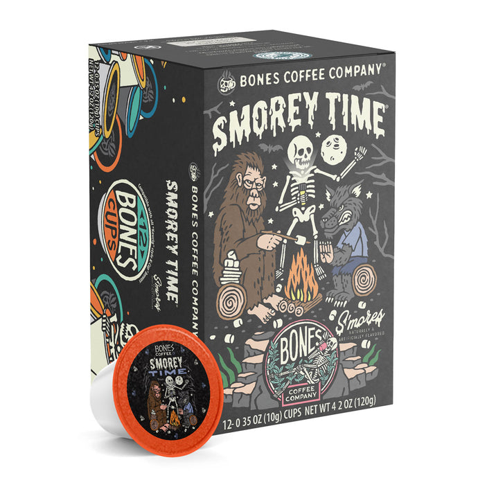 The front of the Bones Coffee Company S’morey Time 12 Count Bones Cups box. Its flavor is s’mores, and it has a skeleton standing up with a flashlight while bigfoot and a werewolf sit nearby beside a campfire on the art.