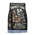 The front of a 12 ounce bag of Bones Coffee Company S’morey Time coffee. Its flavor is s’mores, and it has a skeleton holding a flashlight around a campfire with bigfoot and a werewolf on the art.