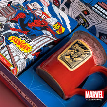 A closeup of the collector's box inspired by Marvel Spider-Man. Inside is a 12 ounce bag of flavored coffee and a red mug with a white glaze on top of it with a golden medallion in its center.