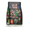 The front of a 12 ounce bag of Bones Coffee Company Sugar Rush coffee. Its flavor is sugar cookie. It has skeletons dressed as elves in a toy workshop on the art.