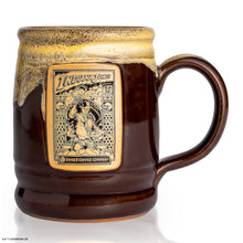 The front of the Bones Coffee Company Toffee Treasure hand thrown mug with Indiana Jones on the golden medallion. It is inspired by Lucasfilm Indiana Jones. The mug is brown colored and has a white glaze on top of it.