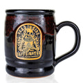 The front of the dead inside mug. It is black colored with a red glaze over it. The medallion shows a skeleton a big mug of coffee in front of them while on fire.