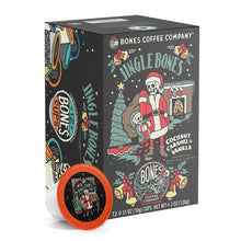 The front of the Bones Coffee Company Jingle Bones 12 Count Bones Cups box. Its flavor is coconut, caramel, and vanilla, and it has two skeletons dressed as Santa Clause and an elf standing inside a living room with a bag over the Santa skeleton’s shoulder on its art.