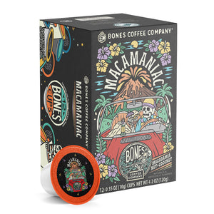 The front of the Bones Coffee Company Macamaniac 12 Count Bones Cups box. Its flavor is a coconut and macadamia nut, and it has a skeleton wearing a cap driving a red car sipping out of a coconut with an erupting volcano behind it on the art.
