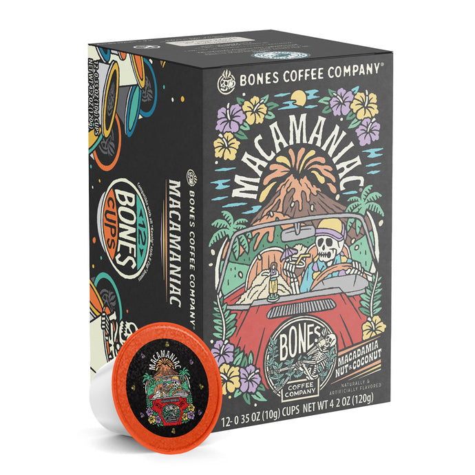 The front of the Bones Coffee Company Macamaniac 12 Count Bones Cups box. Its flavor is a coconut and macadamia nut, and it has a skeleton wearing a cap driving a red car sipping out of a coconut with an erupting volcano behind it on the art.