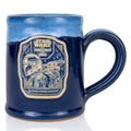 The front of the Bones Coffee Company Beskar Brew Handthrown Mug. It has the Beskar Brew art on the golden medallion. The mug is navy blue colored with light blue and white glaze.