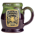 The front of the Bones Coffee Company Mudslide Boogie hand thrown mug with Oogie Boogie from Tim Burton’s The Nightmare Before Christmas on the golden medallion. The mug is plum colored with a kiwi glaze on top.