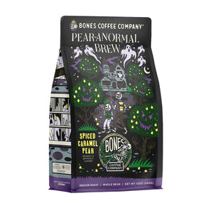 The front of a 12 ounce bag of Bones Coffee Company Pear-anormal Brew coffee. Its flavor is spiced caramel pear, and it has two skeletons walking through a haunted pear orchard towards a house full of ghosts on the art. A sticker says new flavor.
