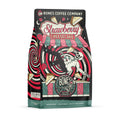 The front of a 12 ounce bag of Bones Coffee Company Strawberry Cheesecake coffee. Its flavor is strawberry cheesecake, and it has a skeleton with a button-down shirt falling into a red and white swirl with cheesecake and strawberries on the art.