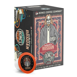 The front of the Bones Coffee Company White Russian 12 Count Bones Cups box. Its flavor is cream and coffee liqueur, and it has a skeleton wearing sunglasses with a goatee in a comfy coat with a white tee shirt holding a cup of coffee on the art.
