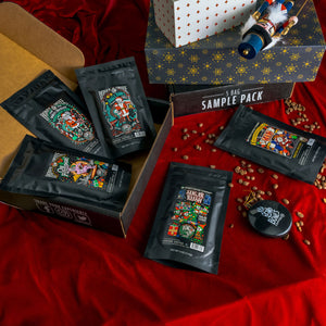 A red table with coffee beans, gifts, a nutcracker, and ornament on top of it. Alongside these items is a 5 Bag Sample Pack box and 5 bags of four ounces of flavored coffee from the Holiday Sample Pack.