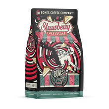 The front of a 12 ounce bag of Bones Coffee Company Strawberry Cheesecake coffee. Its flavor is strawberry cheesecake, and it has a skeleton with a button-down shirt falling into a red and white swirl with cheesecake and strawberries on the art.