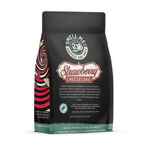 The back of a 12 ounce flavored coffee bag named Strawberry Cheesecake. The Rain Forest Alliance page on the lower left of the back of the bag, and it says to squeeze and sniff at the top of the bag. Below the squeeze and sniff text is the name Strawberry Cheesecake.