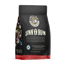 The back of a 12 ounce flavored coffee bag named Sinn-O-Bun. The Rain Forest Alliance page on the lower left of the back of the bag, and it says to squeeze and sniff at the top of the bag. Below the squeeze and sniff text is the name Sinn-O-Bun.