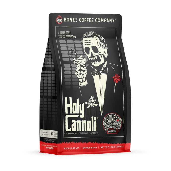 The front of a 12 ounce bag of Bones Coffee Company Holy Cannoli coffee. Its flavor is cannoli, and it has a skeleton wearing a suit with a red rose on the lapel holding a cannoli like a cigar on the art.