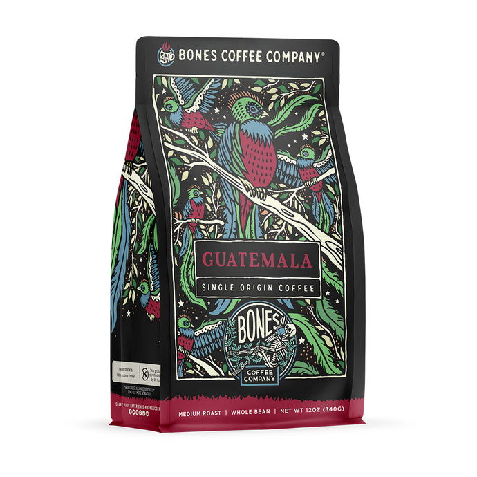 The front of a 12 ounce bag of Bones Coffee Company Guatemala coffee. It has notes of milk chocolate, caramel, and citrus flavors. There is a bird sitting on a branch with other birds flying around on the art.