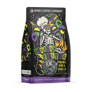The front of a 12 ounce bag of Bones Coffee Company Bananas Foster coffee. Its flavor is banana, rum, and vanilla, and it has a skeleton wearing a chef’s hat and mardi gras glasses with balloons with the New Orleans emblem on the art.