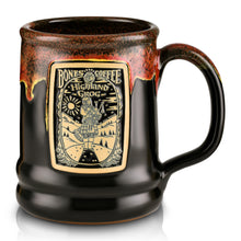 The front of the Bones Coffee Company Highland Grog hand thrown mug with the Highland Grog coffee art on the golden medallion. The mug is black colored and has a sunshine-red glaze on top of it.