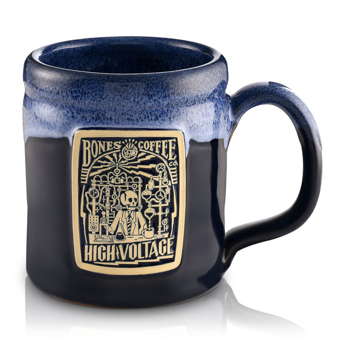 The front of the Bones Coffee Company High Voltage hand thrown mug with the High Voltage coffee art on the golden medallion. The mug is black colored with a blue glaze on top.