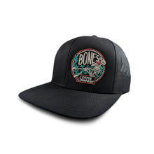 The front of the classic Bones Coffee Company logo trucker hat. The hat is black and the logo has a skeleton sipping coffee sitting on greenery.