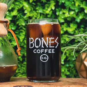 A cold brew glass that has the Bones Coffee Company logo that has the words Bones Coffee Co with the word Bones spelled out with bones. There is coffee inside the cold brew glass.