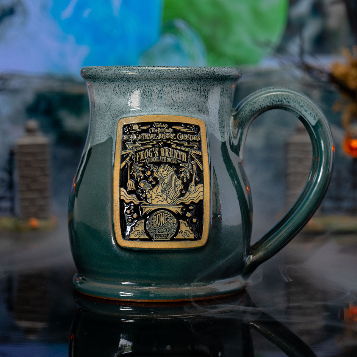 The front of the Bones Coffee Company Frog's Breath hand thrown mug with Sally on the golden medallion. It is inspired by Disney Tim Burton’s The Nightmare Before Christmas. The mug is green colored with a white glaze on top of it. It is inside a foggy toy graveyard.