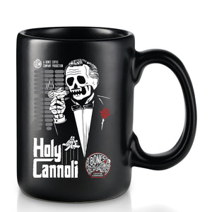 A black mug with the art from the Holy Cannoli coffee on it. It has a skeleton dressed in a black suit with a rose on the lapel holding a cannoli like a cigar.