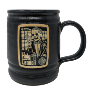 The front of the Bones Coffee Company Holy Cannoli hand thrown mug with the Holy Cannoli coffee art on the golden medallion. The mug is black colored.