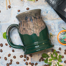 The back of the Irish Cream tankard. It is green colored and has a coffee glaze on top of it. It is on top of a stone surface with coffee beans.
