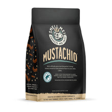 The back of a 12 ounce flavored coffee bag named Mustachio. The Rain Forest Alliance page on the lower left of the back of the bag, and it says to squeeze and sniff at the top of the bag. Below the squeeze and sniff text is the name Mustachio.