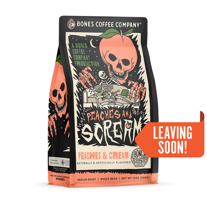 The front of a 12 ounce bag of Bones Coffee Company Peaches and Scream coffee. Its flavor is peaches and cream, and it has a skeleton on a couch in a pair of boxers with peaches on them while a peach with a skeletal face and hands leans down towards them on the art. A sticker says leaving soon.