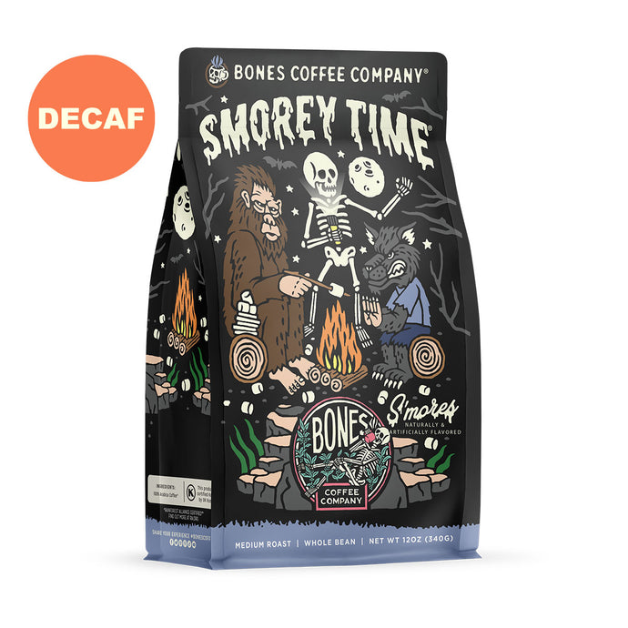 The front of a 12 ounce bag of Bones Coffee Company S’morey Time coffee. Its flavor is s’mores, and it has a skeleton holding a flashlight around a campfire with bigfoot and a werewolf on the art. There is a sticker that says decaf.
