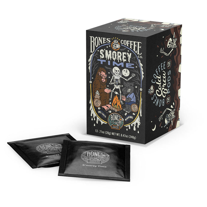 A box and cold brew pods of flavored coffee named S’morey Time. Its flavor is s’mores, and it has a skeleton holding a flashlight around a campfire with bigfoot and a werewolf on the art.