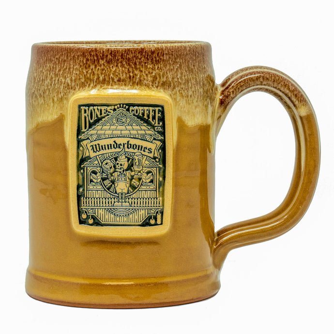 The front of the Bones Coffee Company Wunderbones hand thrown tankard with the Wunderbones coffee art on the golden medallion. The mug is mustard colored with a cinnamon-white glaze on top.