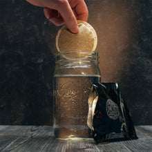 A glass of cold water with an open pack of cold brew pods. Someone is putting the pod into the water.