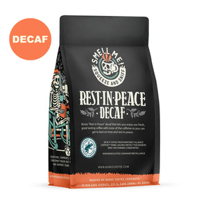 The back of a 12 ounce flavored coffee bag named Rest In Peace. The Rain Forest Alliance page on the lower left of the back of the bag, and it says to squeeze and sniff at the top of the bag. Below the squeeze and sniff text is the name Rest In Peace. A stickers says decaf.